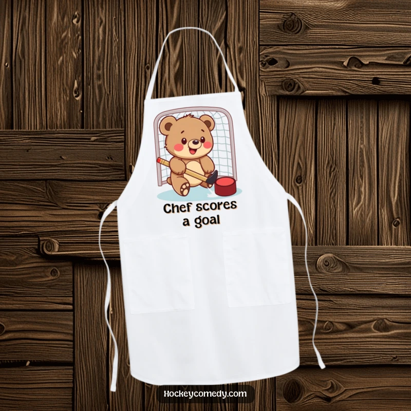 Funny apron showing a bear cub playfully hitting a hockey puck into a net, ready to add sporting fun to cooking.